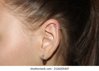 Girl's ear. Ear cartilage piercing + a ring with a scattering of transparent cubic zirkonia and a lobe piercing.