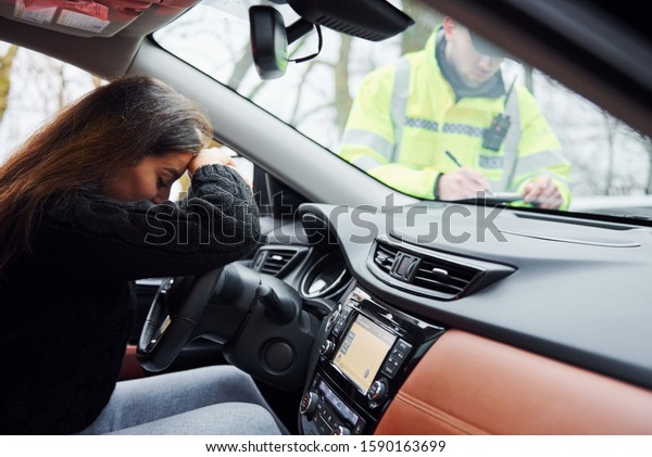 Girls feels bad. Male police officer in green\
uniform checking vehicle on the\
road.