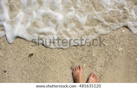 Girl's feet near wave on white sand beach. Sunny afternoon at the tropical island. Barefoot on seashore background image with place for text. Exotic paradise picture from summer vacation