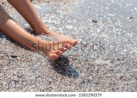 girl's feet on the seashore, waves running over her feet, travel and beach holiday concept