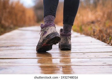 girl's feet walking on wooden boardwalk with hiking boots on rainy day