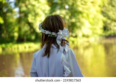 Girl's first Holy Communion, hands folded in prayer. White communion dress, rosary and prayer books, a wreath on the head - Shutterstock ID 2193817363