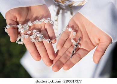 Girl's first Holy Communion, hands folded in prayer. White communion dress, rosary and prayer books, a wreath on the head - Shutterstock ID 2193817377