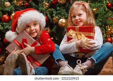 The girls of the girlfriend happily hug the cherished Christmas gifts presented to each other next to the Christmas tree. Gifts given by Santa Claus