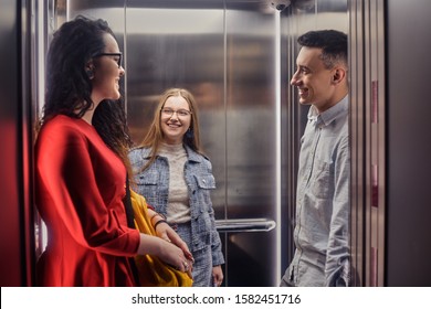 The girls and the guy ride in the elevator. Students go to study. People in the elevator. Elevator with people, communication in public places. Colleagues go to work in the elevator.