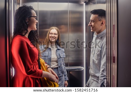 The girls and the guy ride in the elevator. Students go to study. People in the elevator. Elevator with people, communication in public places. Colleagues go to work in the elevator.