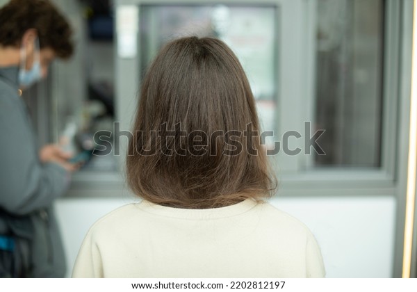 Girls hair from back. Girl in\
line. Brunette on street. White sweater. Uncolored hair on\
head.