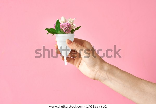 Girl's hand holding
eco friendly soft white silicone menstrual cup with flowers
isolated on pink
background