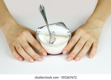 Girl's Hand Holding Plastic Jar With An Open Lid Foil, Natural White Yogurt And Red Jam. Spoon Stuck In The Yogurt. Isolated On White Background