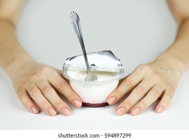 Girl's Hand Holding Plastic Jar With An Open Lid Foil, Natural White Yogurt And Red Jam. Spoon Stuck In The Yogurt. Isolated On White Background.