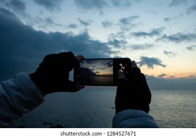 Girl's hand holding smartphone taking sunset photo. Hands in knitted gloves. - Powered by Shutterstock