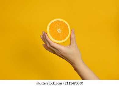 The girl's hand holds a cut round slice of fresh tropical orange. An orange in a woman's hand on a yellow background is isolated. Orange slice. The girl gently holds a citrus in one hand - Powered by Shutterstock