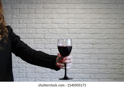 Girl's hand holds a glass of red wine on a white wall background. The harms and benefits of alcohol consumption are a hot topic