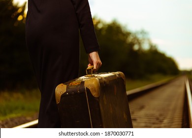 Girl's hand holds an old suitcase in the background railroad