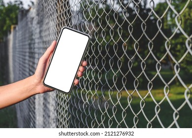 In The Girl's Hand Is A Mock-up Phone. Close-up. Against The Background Of A Steel Wire Fence And Nature