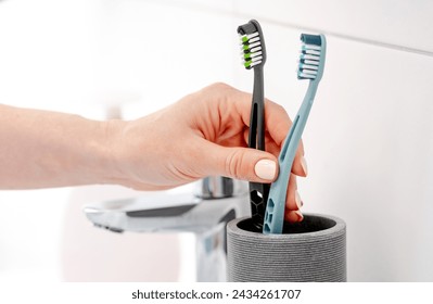 Girl'S Hand Places Two Toothbrushes In Cup For Hygiene In Bright Bathroom - Powered by Shutterstock