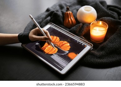 Girl's hand in special glove draws still life picture and pumpkins electronic tablet near burning candle  The concept inspiration  creativity  modern art  Halloween  Thanksgiving day