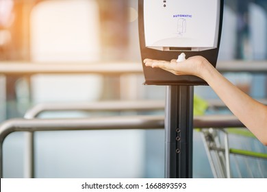 Girl's Hand Under Automatic Foam Dispenser Before Going Inside With Blurred Shopping Cart , In Soft Focus