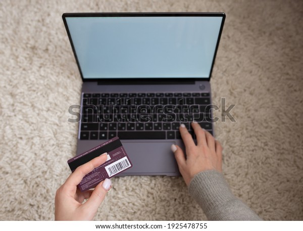 The girl\'s hands hold a credit card, against the\
background of a laptop with a white screen. The girl buys goods\
over the Internet. Online payment. Russia, Altai Territory,\
Barnaul, February 25, 2021