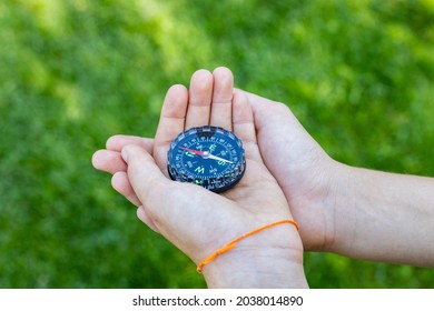 Girl's hands holding the compass. Hands of a teenager girl holding a liquid compass. Red compass needle points north. Green grass background. Copy space. Orienteering on the ground. - Powered by Shutterstock