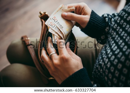 Girl's hands holding euro bills, small money pouch and leather bag