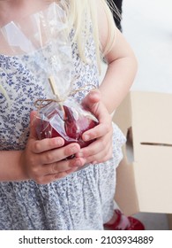 Girl's Hands Holding A Red Candy Apple Wrapped In Cellophane Paper As A Sweet Treat