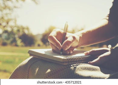 girls hands with pen writing on notebook in park