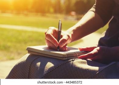 girls hands with pen writing on notebook in park - Shutterstock ID 443485372