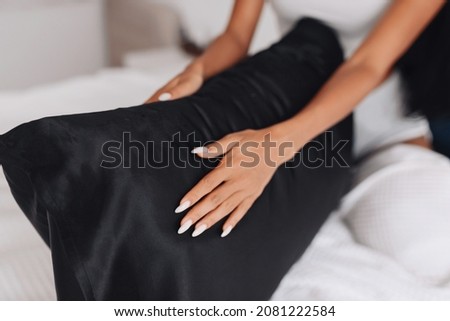 The girl's hands are stroking the pillow with a silk pillowcase. Focus on the pillowcase
