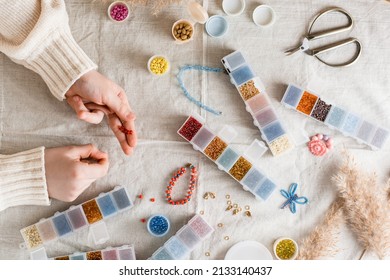 The girl's hands are weaving a beaded bracelet and items for beading on the table. Development of creative skills and fine motor skills for children. Top view.