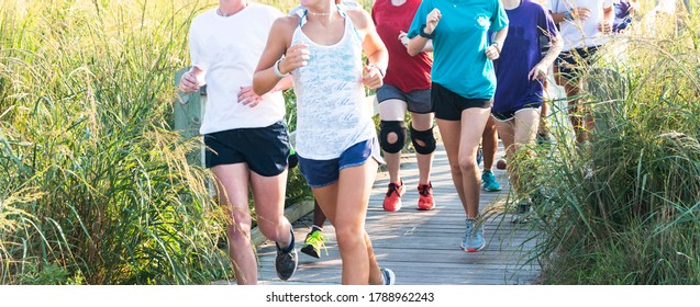 A Girls High School Cross Country Team Is Running Together On A Boardwalk At The Beach Surrounded By Tall Beach Grass.