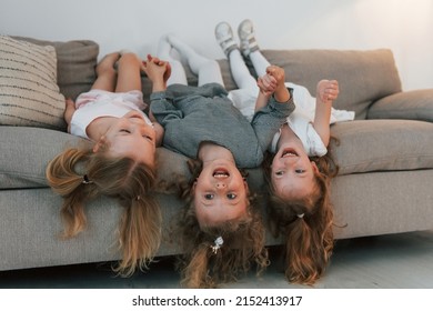 Girls laying down on the sofa upside down and smiling. Group of children is together at home at daytime.