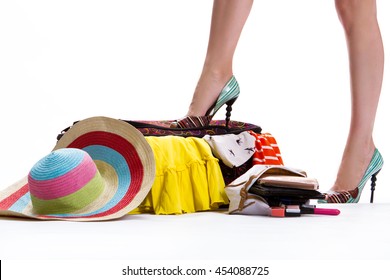 Girl's Leg On Filled Suitcase. Hat Near Closed Filled Suitcase. Luggage For Trip Is Ready. Never Too Much Clothing.