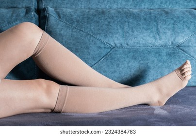 Girl's legs in compression stockings for varicose veins. Pregnancy and varicose veins Legs of a girl at home on the sofa.