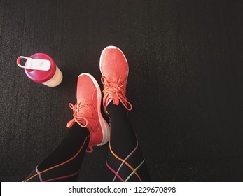 Girls Legs With Shaker Standing Beside On The Black Floor. In The Gym After Workout. Fitness Gear. Sport Shoes.