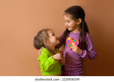 Girls look at each other, holding handmade cards with puzzles in their hand. The eldest child teaches his sister support, care and love by his own example. Symbol of autism day. No discrimination - Shutterstock ID 2135930199