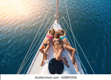 Girls lying on yacht. Smiling ladies wearing swimsuits. Have a happy summer. Today's weather is wonderful.