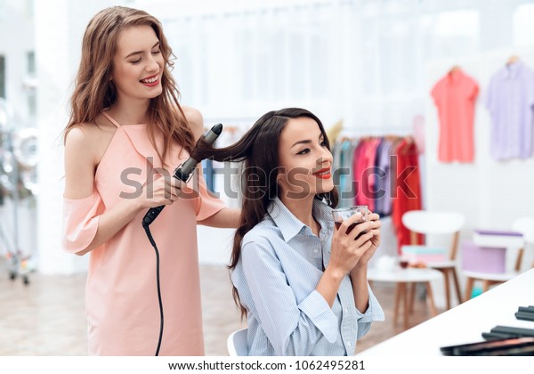 Girls\
make hair styling in the showroom. Girls make hair styling in the\
showroom. Two beautiful girls have fun and\
smile.