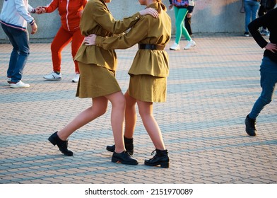 Girls in military uniform learn to dance the waltz on the city embankment on Victory Day in World War II. The concept of celebrating a great victory. Evening. A brass band is playing.