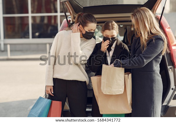 Girls on a\
shopping. People in a masks. Women with a shopping bags. Lady near\
trunk of the car. Coronavirus\
theme.