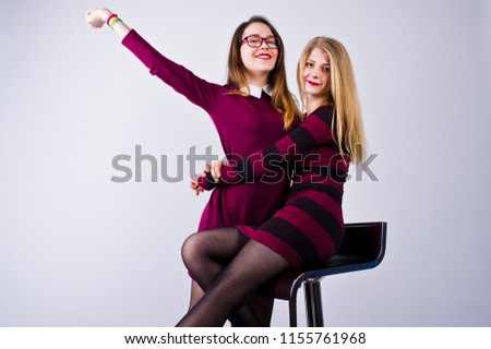 Girls in purple dresses having fun and posing on the chair in the studio.