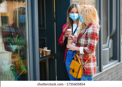 Girls Receiving Coffee From Coffee Shop Outdoors During Quarantine. Two Women In Face Masks Walking City. Friends Travel At City Together. Summer Vacation During Coronavirus Pandemic.