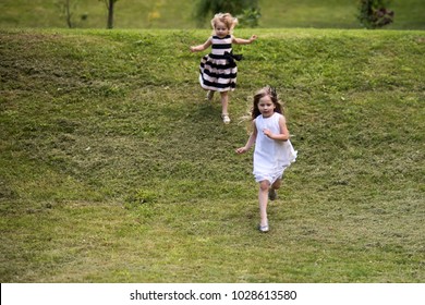 Girls Run From Hill On Green Grass On Summer Day On Natural Landscape. Energy, Energizer, Resilience Concept. Children Playing, Sport, Activity, Fun, Leisure.