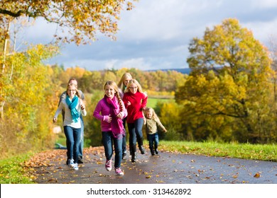 Girls Running Ahead At Family Walk Through The Park In Fall Or Autumn