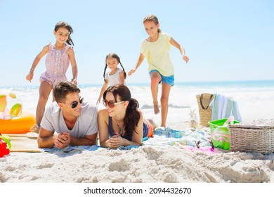 Girls running toward parents laying on beach - Powered by Shutterstock