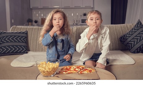 Girls siblings eat together popcorn and pizza and watch interesting movie. Sisters enjoy watching movie at home and eating yummy food together, toned - Powered by Shutterstock