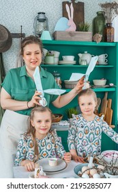 Girls, Sisters, Mother At Table With Easter Decoration. Celebration In Kitchen.Tablescape For Home Easter Holiday.Family Religious Traditional Festive Food, Meal. Colored Eggs,cake, Fun, Bunny Ears.