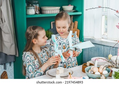 Girls, Sisters At Table With Easter Decoration. Celebration In Kitchen.Tablescape For Home Easter Holiday.Family Religious Traditional Festive Food, Meal. Colored Eggs,cake, Funny Bunny, Candy Sweet.