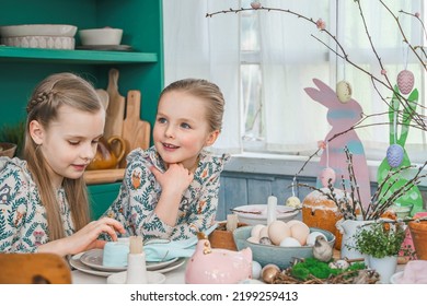 Girls, Sisters At Table With Easter Decoration. Celebration In Kitchen.Tablescape For Home Easter Holiday.Family Religious Traditional Festive Food, Meal. Colored Eggs,cake, Funny Bunny, Candy Sweet.