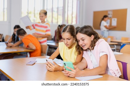 Girls sitting at desk in classroom, using smartphones together during lesson in school. - Powered by Shutterstock